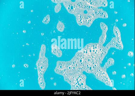Mousse de savon sur fond turquoise. Bulles de mousse à laver et points blancs sur la surface colorée. Texture mousse de shampooing. Mise au point sélective. Banque D'Images