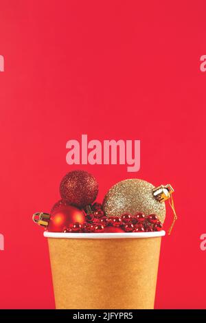 Fond de Noël vertical rouge avec une tasse à café en carton pleine de décorations pour arbres de Noël. Placer pour le texte. Banque D'Images
