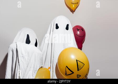 Joyeux Halloween. Enfants vêtus de costumes blancs fantômes et de boules orange peintes avec des stylos feutre. Différentes émotions de joie, de colère, de rire. Décoration de fête, le concept de fête à la maison. Banque D'Images