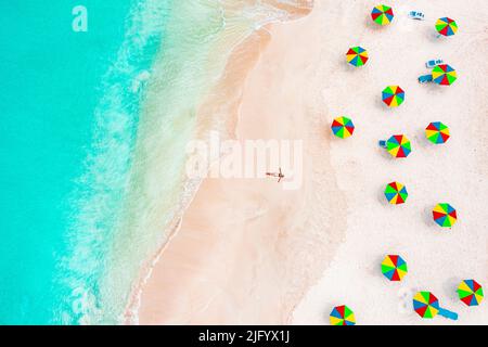 Vue aérienne de la femme en bikini bains de soleil sur une plage tropicale à côté de parasols colorés, Antigua, Antilles, Caraïbes, Amérique centrale Banque D'Images