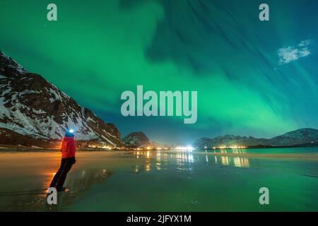 Randonneur à la torche de tête regardant l'Aurora Borealis (aurores boréales) se tenant sur la plage de Ramberg, dans le comté de Nordland, dans les îles Lofoten, en Norvège, en Scandinavie Banque D'Images