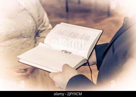 Anneaux de mariage sur une Bible présentée par le prêtre à la mariée et au marié de jeunes mariés lors de la cérémonie de mariage dans une église Banque D'Images