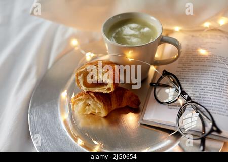 croissants, thé au matcha, livre et verres au lit Banque D'Images