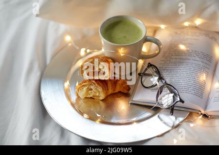 croissants, thé au matcha, livre et verres au lit Banque D'Images