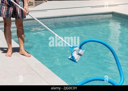 Homme méconnaissable nettoyant la piscine avec un nettoyeur automatique de piscine à son arrière-cour de maison Banque D'Images