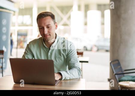 Jeune homme d'affaires assis dans un café travaillant avec un ordinateur portable Banque D'Images