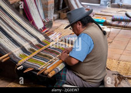 Equateur, Quito, Paguche. Atelier de tissage Tahuantinsuyo. Démonstration traditionnelle de tissage « back strap ». Tisserand dans une tenue locale typique. Banque D'Images