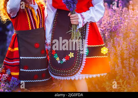 Belles filles en costumes traditionnels de folklore bulgare dans le champ de lavande pendant la récolte et le coucher du soleil Banque D'Images