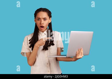 Femme stupéfait d'être choquée des problèmes de logiciels opérationnels, pointant vers l'écran d'ordinateur portable, afraides de perte de données, portant une chemise blanche. Studio d'intérieur isolé sur fond bleu. Banque D'Images