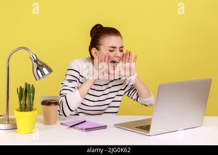 Une femme nerveuse en colère travaillant dans une chemise rayée criait bruyamment les mains près de la bouche, parlant vidéo conférence assis sur le lieu de travail. Studio d'intérieur tourné isolé sur fond jaune. Banque D'Images