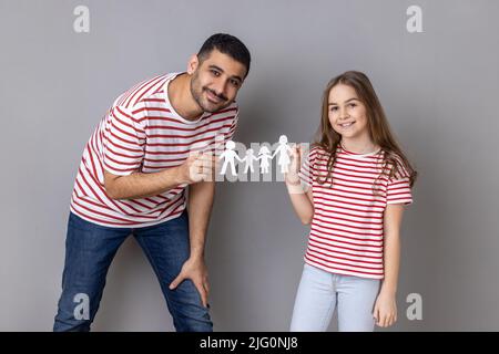 Portrait du père et de la fille tenant ensemble les gens de la chaîne de papier, famille heureuse, relations, enfance, parentalité, regarder l'appareil photo avec le sourire. Prise de vue en studio isolée sur fond gris. Banque D'Images