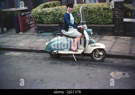 1960s, historique, une jeune femme, avec un style de cheveux de l'époque, assis sur un scooter Lambretta garée à côté d'un trottoir dans une rue de banlieue, Londres, Angleterre, Royaume-Uni. Conçu comme un véhicule simple, robuste et abordable, le scooter avait un carénage de guidon (protection) et un porte-bagages arrière en métal. Avec le moteur monté sur la roue arrière, un siège pillon arrière et un simple changement de vitesse de guidon, la zone de passage a été conçue pour les femmes, car le port d'une robe ou d'une jupe sur une moto traditionnelle n'était pas vraiment possible. À cette époque, ils étaient souvent appelés scooters « Mod ». Banque D'Images