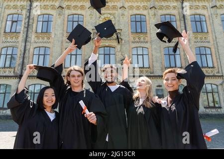 Des diplômes et des chapeaux de jeune fille souriants et multiethniques sont à l'extérieur Banque D'Images