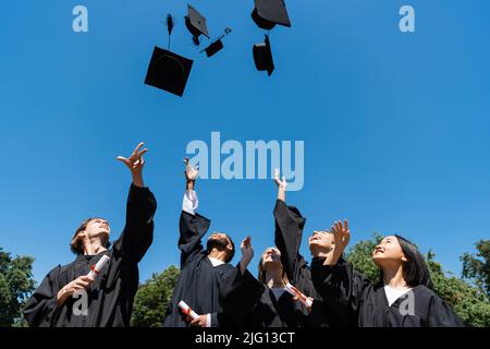 Baccalauréat interracial avec des diplômes de projection de casquettes avec le ciel à l'arrière-plan Banque D'Images