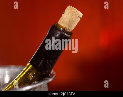 Gros plan du col d'une bouteille de vin avec un liège dans des gouttes d'eau sur fond rouge Banque D'Images