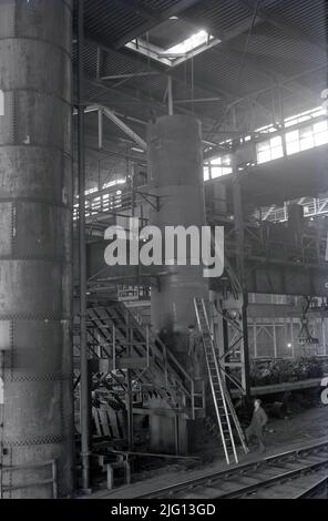 1950s, historique, deux sidérurgistes, l'un sur une échelle, à l'intérieur d'un hangar géant en acier avec la piste rali à Abbey Works, Port Talbot, pays de Galles, Royaume-Uni, le site de la compagnie d'acier du pays de Galles, à cette époque, le plus grand producteur d'acier en Europe. Banque D'Images