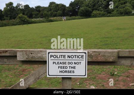 Panneau sur une porte de ferme disant poli avis s'il vous plaît ne pas nourrir les chevaux. Un cheval peut être vu en arrière-plan Banque D'Images