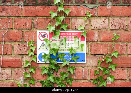 Danger tenir à l'extérieur et panneau d'avertissement de danger sur le mur de brique rouge avec la lierre verte qui grandit Banque D'Images