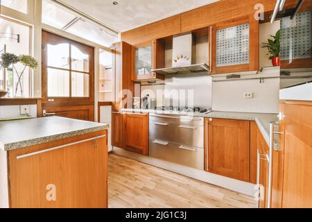 Décoration intérieure moderne d'une cuisine d'angle avec des armoires en bois marron et une hotte au-dessus de la cuisinière dans un appartement moderne Banque D'Images