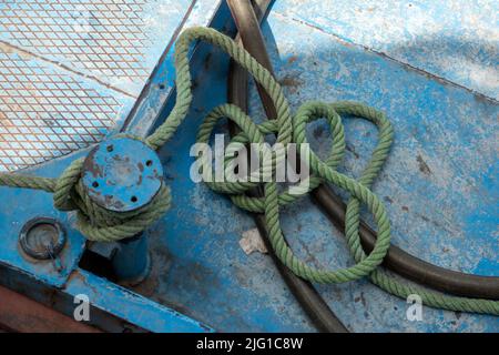 Une courte longueur de corde d'amarrage vert pâle attachée à un petit bollard sur le pont d'un navire peint en bleu pâle Banque D'Images