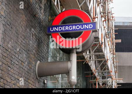 Londres, Royaume-Uni - 01 février 2019: Panneau de métro rouge et bleu typique au mur de brique, échafaudage de construction en arrière-plan Banque D'Images