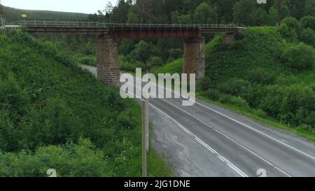 Vue de dessus du pont avec la route sous elle en forêt. Scène. Vieux pont sur l'autoroute rurale dans la zone boisée. Pont avec routes dans la région boisée et vallonnée en su Banque D'Images