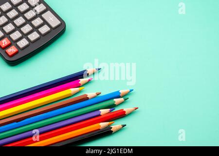Gros plan d'un tas de crayons de couleur et de calculatrices noires sur une table verte. Banque D'Images