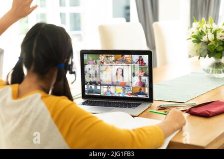 Vue arrière d'une fille caucasienne levant la main en classe en ligne pendant un appel vidéo sur ordinateur portable à la maison Banque D'Images