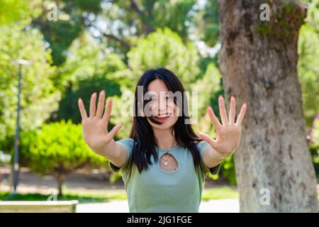 Bonne femme brune portant un t-shirt turquoise sur le parc de la ville, en plein air montrant et pointant vers le haut avec les doigts numéro dix tout en souriant confiant et heureux. S Banque D'Images