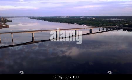 Vue aérienne d'un long pont au-dessus de la rivière large au coucher du soleil. Attache. Campagne avec une rivière calme près du village Banque D'Images