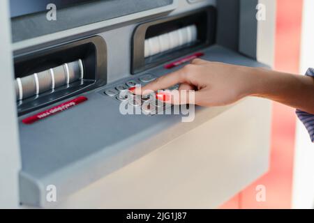 Jeune femme brune portant une chemise rayée bleue sur le parc de la ville, à l'extérieur en utilisant un distributeur automatique de billets pour retirer son argent. Banque D'Images