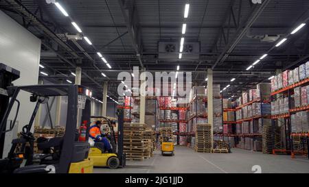 Moscou - Russie, 04.20.2022 : chariot élévateur se déplaçant entre de grandes étagères métalliques dans un entrepôt moderne et chargeant des palettes avec des marchandises. Créatif. Travailleurs Banque D'Images