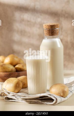 Un verre et un pot de lait de pomme de terre avec des pommes de terre crues dans un bol. Banque D'Images