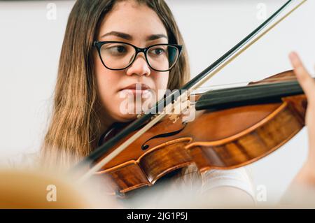 jeune femme caucasienne avec des lunettes, assise sur le canapé à la maison pratiquant le violon en regardant les doigts sur le fretboard du violon, pratiquant le classique Banque D'Images