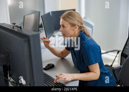 L'infirmière en service fait une annonce dans le microphone assis à la réception dans une clinique moderne Banque D'Images