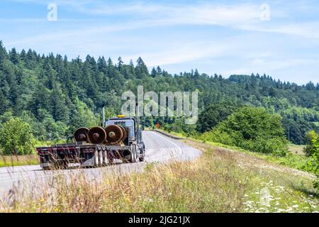 Tracteur semi-remorque noir de Big RIG avec feux clignotants jaunes sur le toit pour indiquer le transport de charge surdimensionnée en marche avec semi-trai à marchepied chargé Banque D'Images