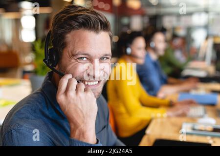 Portrait du responsable du service clientèle homme caucasien souriant avec casque au bureau Banque D'Images