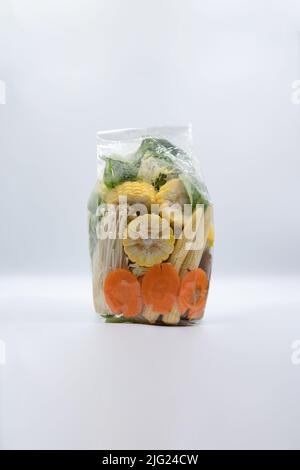 Les carottes, les légumes, le maïs et les champignons à aiguille dorés sont prêts à être vendus dans des sacs en plastique transparents sur fond blanc. Banque D'Images