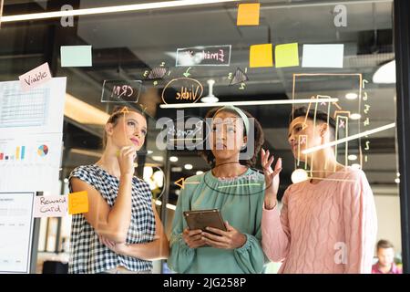 Des collègues multiraciaux remue-méninges du plan d'affaires sur un mur de verre au bureau Banque D'Images