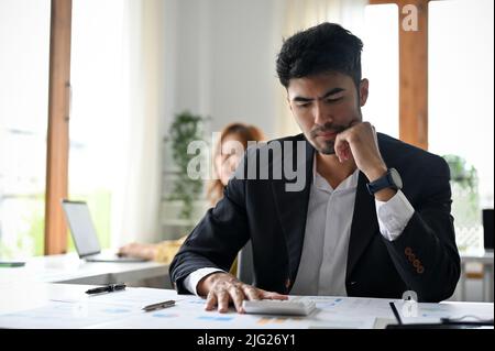 Un homme d'affaires ou un directeur de sexe masculin élégant et professionnel, jeune adulte asiatique, pense sérieusement à un projet d'entreprise à son bureau. Banque D'Images