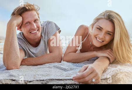 Portrait d'un jeune couple heureux allongé sur une couverture et profitant de vacances à la plage. Jeune homme blond souriant et femme se détendant sur la plage et appréciant leur Banque D'Images