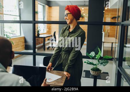 Bonne femme d'affaires musulmane qui a une réunion avec ses collègues dans une salle de réunion moderne. Femme entrepreneure gaie portant un foulard dans un multisegment Banque D'Images