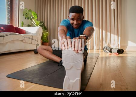 Un jeune homme afro-américain noir s'entraînant à la maison, étirant ses jambes avant de s'exercer sur son tapis de yoga et de suivre un cours en ligne Banque D'Images