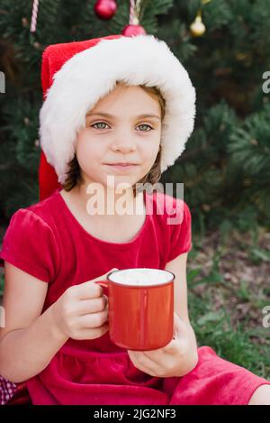 Joyeux Noël. Portrait de drôle d'enfant fille dans le chapeau de Santa manger des biscuits de pain d'épice boire du chocolat chaud à l'extérieur d'avoir du plaisir. Joyeuses fêtes. Enfant en vacances. Noël en juillet Banque D'Images
