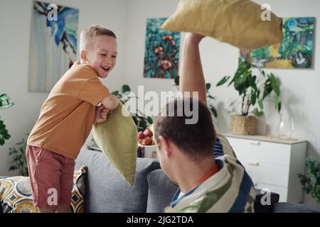 Joyeux petit fils, jouant à l'oreiller de combat avec son père sur le canapé pendant les loisirs à la maison Banque D'Images