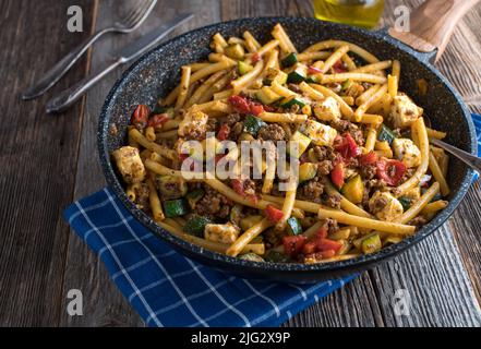 Plat de macaroni au bœuf haché, aux légumes et au fromage feta dans une poêle isolée sur une table en bois. Banque D'Images