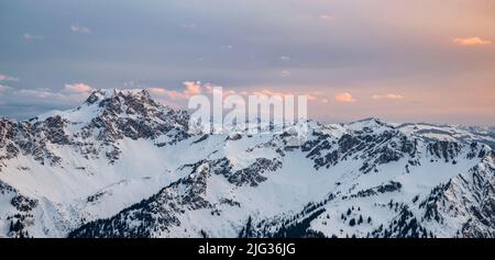 Des nuages colorés sur une chaîne de montagnes enneigée au coucher du soleil en hiver. Allgau Alpes, Bavière, Allemagne Banque D'Images