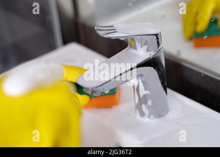 Enfilez des gants en caoutchouc jaune tenant une éponge pour laver le robinet sale avec du tartre Banque D'Images