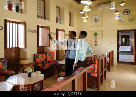 Deux visiteurs indiens prennent un selfie dans un salon arabe traditionnel. Chaises en bois avec coussins colorés. Les assiettes et les bols décorent le mur. Banque D'Images