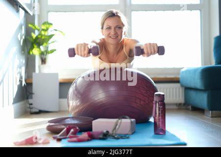 La jeune femme est engagée dans la forme physique avec des haltères sur le fitball à la maison Banque D'Images